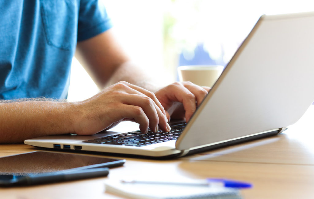 Mann sitzt am Schreibtisch und schreibt auf dem Laptop